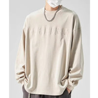 メンズ長袖Tシャツ。ゆったりしたオフホワイトのクルーネックで、胸元に同色の立体ロゴ入り