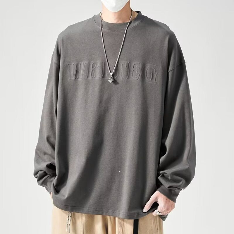 メンズ長袖Tシャツ。ゆったりしたグレーのクルーネックで、胸元に同色の立体ロゴ入り